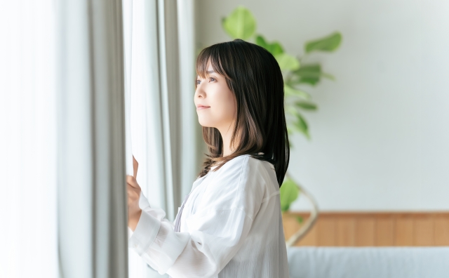 主婦がカーテンを開けて日光を浴びている様子